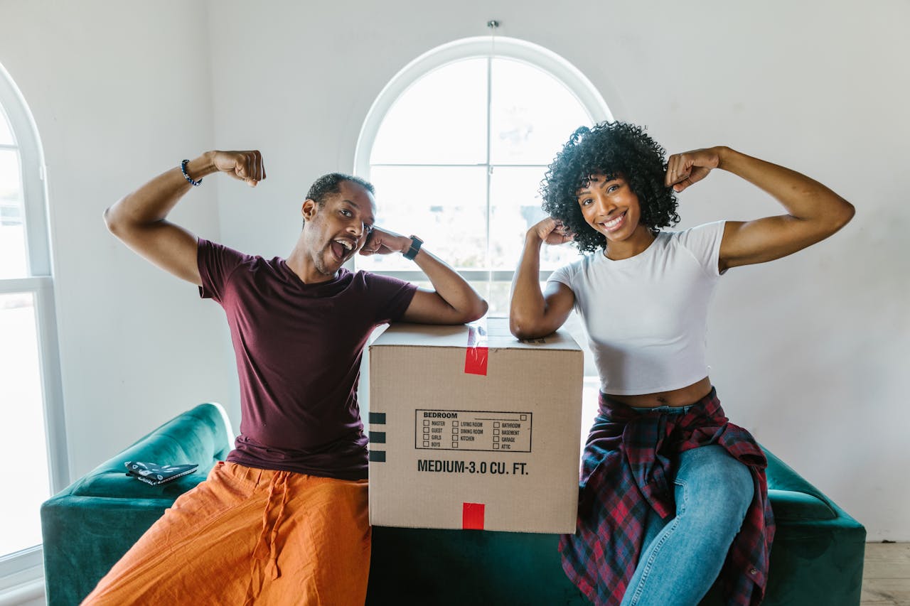 Joyful couple flexing muscles while unpacking in their new home.